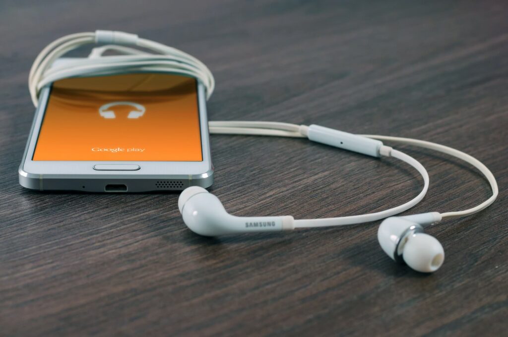white Samsung Android smartphone turned beside white earbuds on brown desk